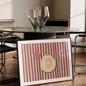 Puede incluir: Impresi&oacute;n art&iacute;stica enmarcada que representa un desayuno: tostadas con mantequilla, mermelada y un cuchillo, sobre un fondo a rayas rosas y marrones. Dos jarrones de cristal decorativos sobre una mesa de m&aacute;rmol. Marco negro.