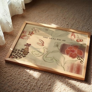 Puede incluir: Una impresi&oacute;n art&iacute;stica enmarcada con un marco de madera clara. La obra presenta ilustraciones de cisnes, flores y otros elementos decorativos en tonos rojos, beige y marr&oacute;n. El texto "HOW LUCKY ARE WE" es visible.