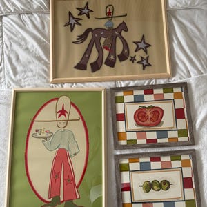 May include: Four framed art pieces. One features a figure on a horse with stars, another depicts a person holding a tray with drinks, and two others show a tomato and olives. The frames are various colors.