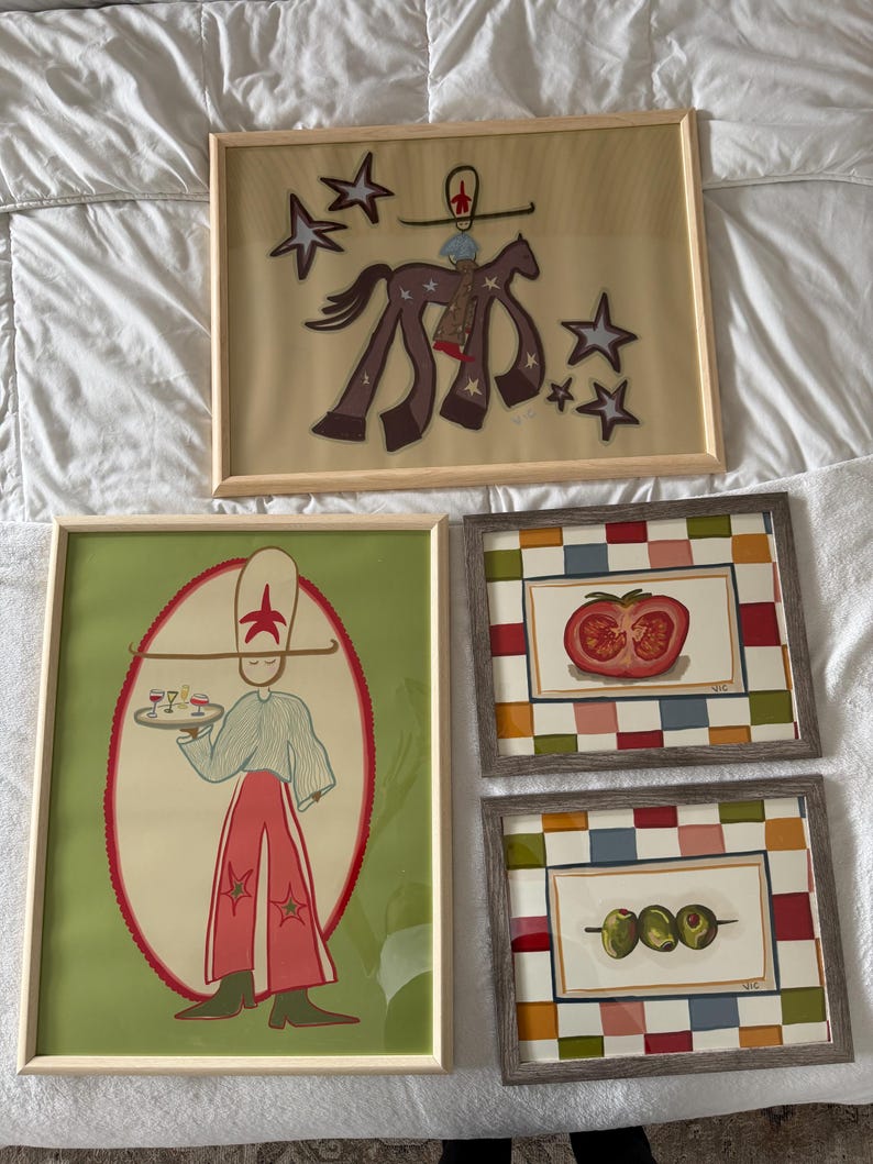 May include: Four framed art pieces. One features a figure on a horse with stars, another depicts a person holding a tray with drinks, and two others show a tomato and olives. The frames are various colors.