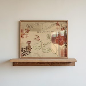 Puede incluir: Una obra de arte enmarcada con un fondo dorado, que muestra ilustraciones dibujadas a mano de cisnes, flores y cerezas. El texto "HOW LUCKY ARE WE" est&aacute; escrito en la parte superior. La obra de arte se exhibe en una estanter&iacute;a de madera.
