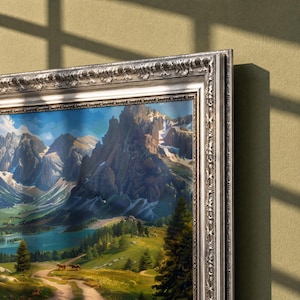 May include: A landscape painting in a decorative silver frame featuring a mountain range with snow-capped peaks, a blue lake, and a green valley with a dirt path and two small animals. The artwork displays a bright sky and dense pine trees.