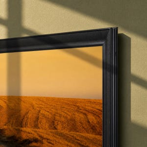 May include: A rectangular wall art piece featuring a landscape of a golden wheat field under a warm orange sky, enclosed within a thick, matte black frame with a multi-layered, stepped profile design that adds depth to the overall presentation.