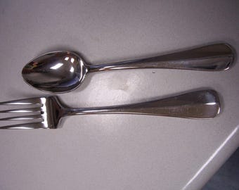 May include: A stainless steel spoon and fork set. The spoon has a rounded bowl and a long handle. The fork has four tines and a matching handle. Both utensils are reflective and appear to be made of metal.