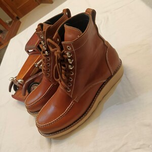 May include: A pair of brown leather boots with a lace-up design and white stitching. The boots have a rounded toe and a thick, light-colored sole. The boots are approximately 6 inches tall.