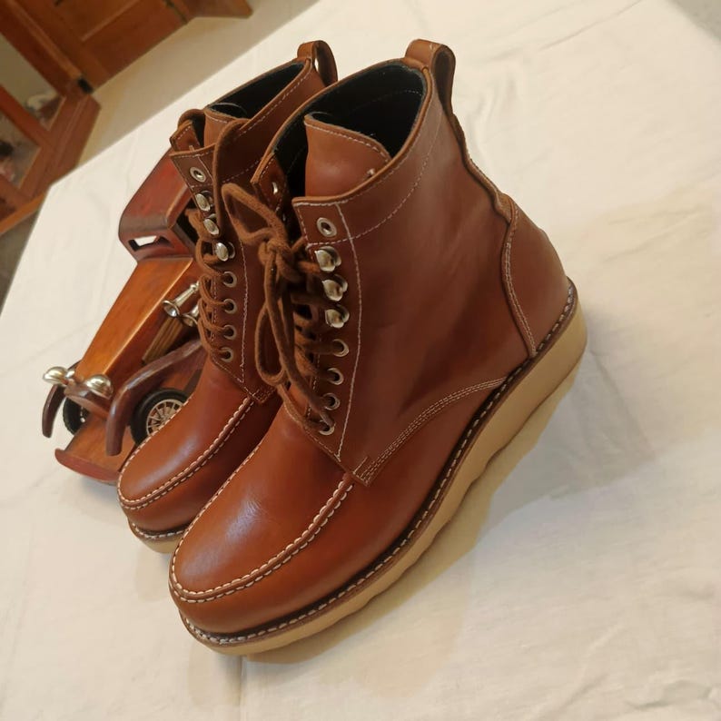 May include: A pair of brown leather boots with a lace-up design and white stitching. The boots have a rounded toe and a thick, light-colored sole. The boots are approximately 6 inches tall.