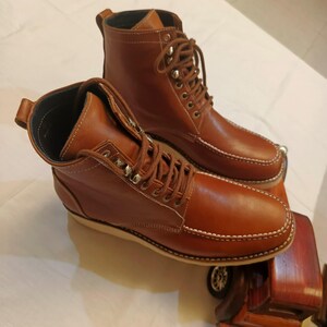 May include: A pair of brown leather boots with a classic design. The boots feature a lace-up closure, metal eyelets, and white stitching along the soles. The boots are made of a smooth, polished leather and have a sturdy construction.