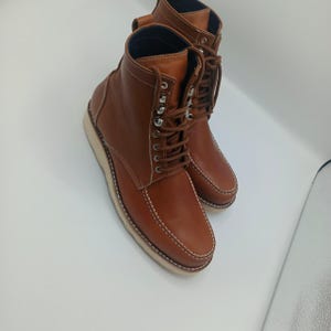 May include: A pair of brown leather boots with a lace-up design. The boots have a light-colored sole and white stitching. The boots are a classic style, suitable for various occasions.