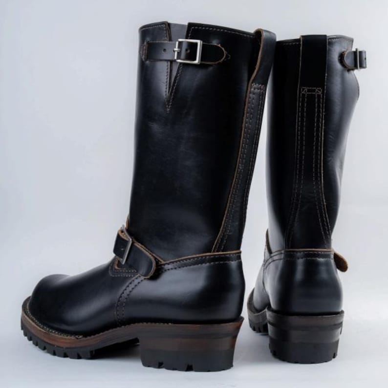 May include: A pair of black leather motorcycle boots with buckle closures. The boots have a tall shaft, a rounded toe, and a thick, dark brown sole. The boots are approximately 12 inches tall.