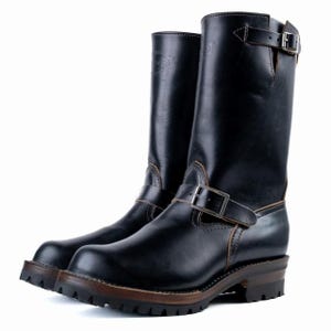 May include: Black leather motorcycle boots with a buckle closure and a lug sole. The boots have a tall shaft and a brown sole. The leather has a glossy finish. The boots are designed for durability and style.