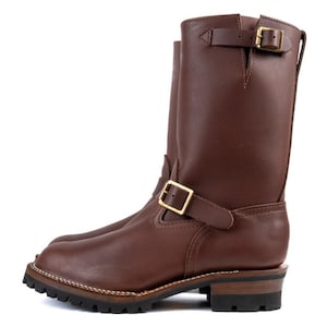 May include: Brown leather motorcycle boots with a square toe and a lug sole. The boots have two adjustable straps with gold-colored buckles. The shaft of the boot is approximately 10 inches high.