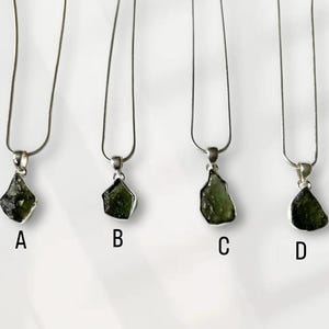May include: Four silver necklaces, each with a green gemstone pendant, labelled A, B, C, and D. The pendants vary in shape and size. The gemstones are dark green and set in silver. The necklaces are shown against a white background.