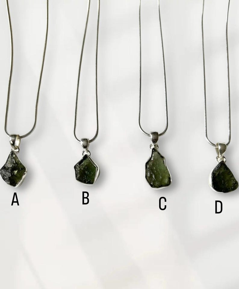 May include: Four silver necklaces, each with a green gemstone pendant, labelled A, B, C, and D. The pendants vary in shape and size. The gemstones are dark green and set in silver. The necklaces are shown against a white background.