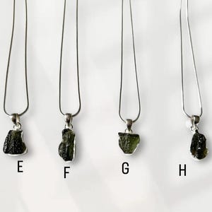 May include: Four silver necklaces, each featuring a green, rough-cut pendant. The pendants are suspended from fine silver chains. The pendants are labelled E, F, G, and H.