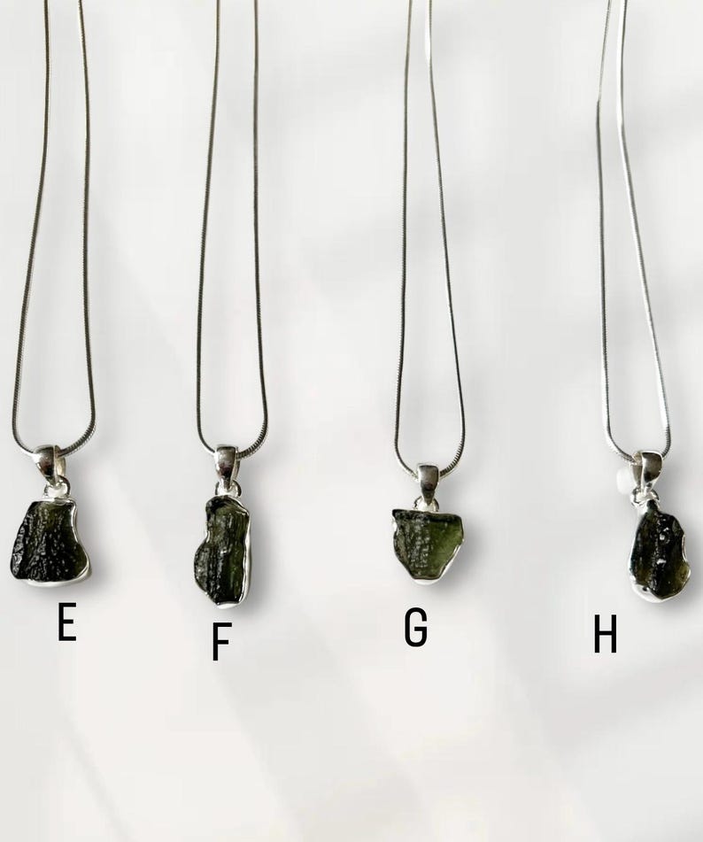 May include: Four silver necklaces, each featuring a green, rough-cut pendant. The pendants are suspended from fine silver chains. The pendants are labelled E, F, G, and H.