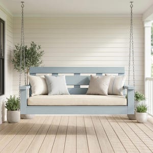 May include: A light blue wooden porch swing with a beige cushion and four decorative pillows. The swing is suspended by metal chains and is surrounded by potted plants, creating a relaxing outdoor seating area.