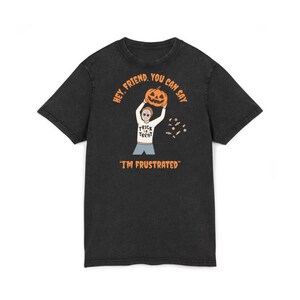 Puede incluir: Camiseta negra con un diseño temático de Halloween. El diseño presenta una figura de dibujos animados sosteniendo una calabaza tallada, con el texto "HEY, FRIEND, YOU CAN SAY" arriba y "I'M FRUSTRATED" abajo. También se muestran caramelos.