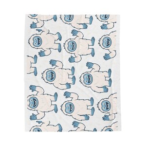 May include: White blanket with a repeating pattern of cartoon yeti characters. Each yeti has a light pink body, blue face, and blue hands and feet. The yeti are smiling and lying down.