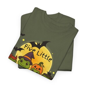 May include: Two olive green t-shirts are folded and stacked. The top shirt features a Halloween-themed graphic with the text "Five Little" above a cartoon turtle wearing a witch hat, a pumpkin, and a full moon.
