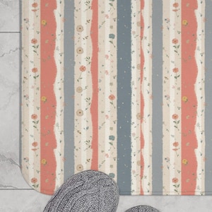 May include: A rectangular bath mat with a striped pattern in coral, light blue, and cream colors. The stripes are vertical and have a floral design. Two gray knitted slippers are at the bottom of the mat.