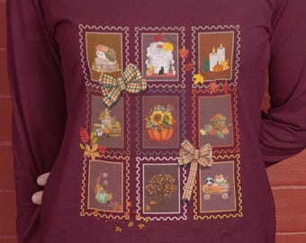 May include: Burgundy long-sleeve shirt with a square pattern of fall-themed illustrations. The illustrations include pumpkins, bows, and autumn leaves. The person is wearing blue jeans.