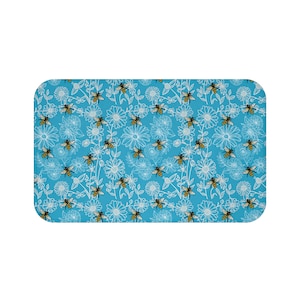 May include: A rectangular, light blue mat with a repeating pattern of white flowers and yellow and black bees. The flowers have a simple, outlined design. The bees are depicted with detailed wings and stripes.