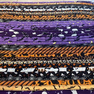 May include: Oval Halloween-themed rug made from fabric strips. The rug has orange, black, and purple stripes with Halloween patterns such as bats, ghosts, and spiderwebs. A decorative item for the home.