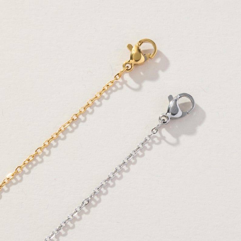 May include: Two delicate metal chains, one in a polished gold tone and one in a bright silver tone. Each chain features a small, functional lobster claw clasp at the end, designed for securing jewelry pieces with a simple and reliable mechanism.