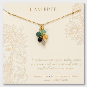 May include: A gold chain necklace featuring a cluster of five small, faceted gemstone beads in green, black, yellow, and grey. The display card reads I AM FREE and lists the stones as aventurine, indian agate, citrine, onyx, and labradorite.