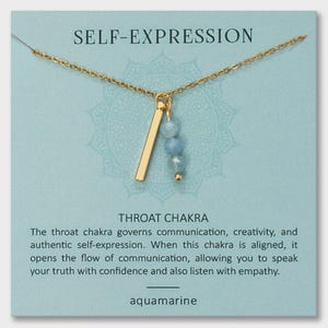 May include: Gold-colored necklace with a pendant featuring a vertical bar and three aquamarine beads. The necklace is displayed on a light blue card with the words "SELF-EXPRESSION" and "THROAT CHAKRA". The card also includes text about the throat chakra.