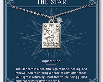 Può includere: Una collana d'argento con un ciondolo raffigurante il design della carta dei tarocchi "THE STAR". Il ciondolo presenta un'illustrazione dettagliata ed è accompagnato da una piccola perla di acquamarina. La collana è esposta su uno sfondo blu scuro.