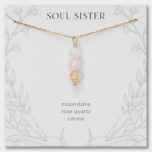 May include: A gold chain necklace with a pendant featuring three stacked beads: a white moonstone, a pale pink rose quartz, and a yellow citrine. The necklace is displayed on a white card labeled SOUL SISTER with moonstone, rose quartz, and citrine text.