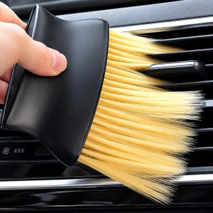 Könnte beinhalten: Eine schwarze Kunststoff-Reinigungsbürste für Auto-Lüftungsschlitze mit einem geschwungenen Griff und langen, weichen, hellgelben Borsten, die dazu dient, in die schmalen Zwischenräume der horizontalen Lamellen der Lüftung zu gelangen.