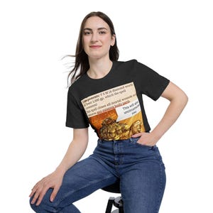 May include: Dark gray t-shirt featuring a humorous graphic with text about a spell that closes wounds and restores body parts. The text is in a speech bubble and a rectangular box. The shirt is paired with blue jeans.
