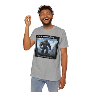 May include: A grey t-shirt with a black graphic of a large, hairy creature standing in a mountainous landscape. The text on the graphic reads "The 4 most terrifying Words A DM can utter: You can certainly try..."
