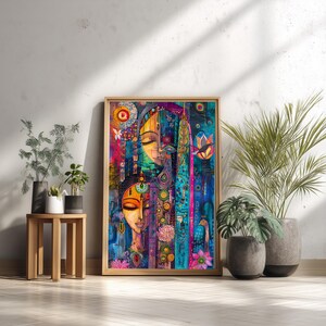 May include: A framed artwork depicting two stylized faces with closed eyes, in vibrant colours. The artwork uses teal, pink, yellow, and purple hues, with floral and geometric patterns. The artwork is leaning against a white wall, next to potted plants.