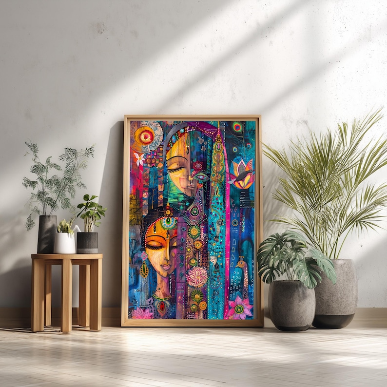 May include: A framed artwork depicting two stylized faces with closed eyes, in vibrant colours. The artwork uses teal, pink, yellow, and purple hues, with floral and geometric patterns. The artwork is leaning against a white wall, next to potted plants.