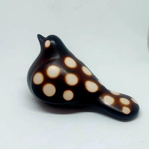 May include: A ceramic bird ornament. The bird has a dark brown body with cream-coloured polka dots. The bird is in a perched position, with its head tilted upwards. A decorative item.