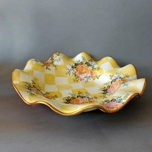 May include: A decorative ceramic serving dish with a wavy edge. The dish features a yellow and white checkered pattern, with floral rose accents. The rim is trimmed with gold paint. The dish is approximately 30 cm in diameter.