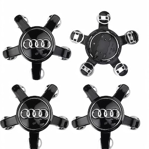 May include: Four black and silver Audi wheel center caps. Each cap features the Audi logo in silver against a black background. The caps have a star-like design with five silver accents. One cap is shown from the back.