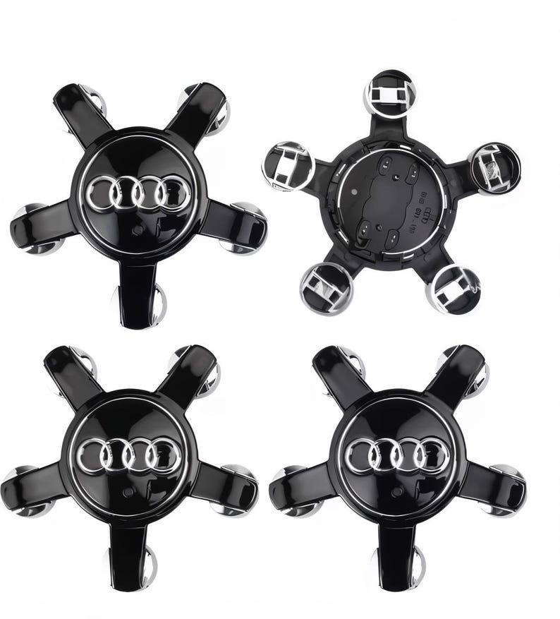 Puede incluir: Cuatro tapacubos Audi negros y plateados. Cada tapacubo presenta el logotipo de Audi en plata sobre un fondo negro. Los tapacubos tienen un dise&ntilde;o en forma de estrella con cinco detalles plateados. Se muestra un tapacubo desde atr&aacute;s.