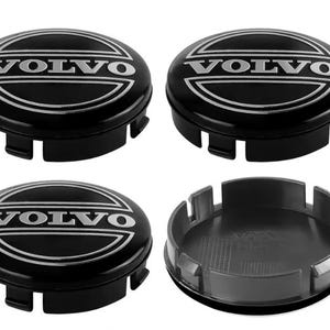 May include: Four black Volvo center caps. Each cap has the Volvo logo in silver lettering and a silver outline. One cap is shown disassembled, revealing the interior. The caps have a circular design with tabs for secure attachment.