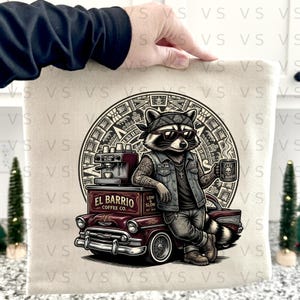 Könnte beinhalten: Beige Tragetasche mit einem Waschbären mit Sonnenbrille, Bandana und Jeansweste. Der Waschbär lehnt an einem Oldtimer mit dem Text "El Barrio Coffee Co.". Eine Kaffeemaschine und eine Kaffeetasse sind ebenfalls zu sehen.