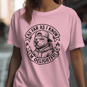 Könnte beinhalten: Hellrosa T-Shirt mit einer schwarz-weißen Grafik eines Hundes mit Kappe und Kapuzenpullover. Die Grafik enthält den Text "AS FAR AS I KNOW I'M DELIGHTFUL" in einem kreisförmigen Design. Das T-Shirt ist einfarbig rosa.