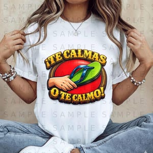 以下が含まれることがあります： 白いTシャツ。緑と青のビーチサンダルが手で持たれ、赤い円を背景にしたグラフィック。テキスト「¡TE CALMAS O TE CALMO!」がグラフィックの上と下に表示されています。