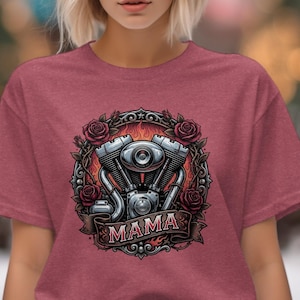 May include: Maroon t-shirt featuring a motorcycle engine graphic with the word "MAMA" on a banner. The design includes roses and flames, creating a biker-themed aesthetic. The shirt is made of a soft material.