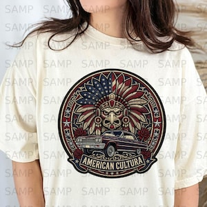 Puede incluir: Camiseta color crema con un diseño gráfico circular. El diseño presenta un diseño de tocado de águila en rojo, blanco y azul, y un coche clásico. El texto "AMERICAN CULTURA" se muestra en una pancarta.