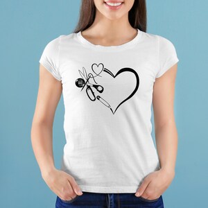 Op de afbeelding: Wit T-shirt met een zwarte afbeelding van een hart met naai-attributen. Het ontwerp bevat een schaar, een knoop, een naald en een speld. Het shirt is gemaakt van een zacht materiaal, geschikt voor naaisters.