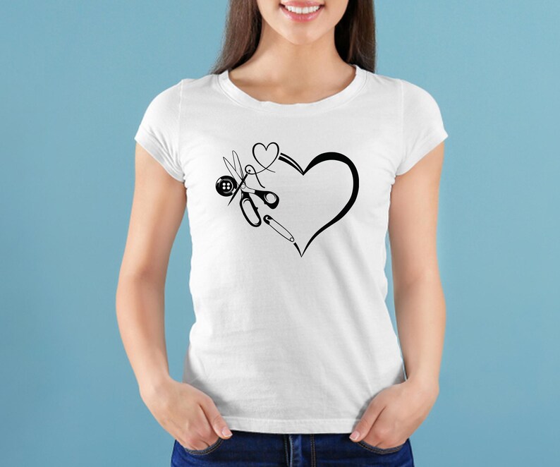 Op de afbeelding: Wit T-shirt met een zwarte afbeelding van een hart met naai-attributen. Het ontwerp bevat een schaar, een knoop, een naald en een speld. Het shirt is gemaakt van een zacht materiaal, geschikt voor naaisters.