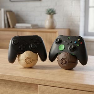 Könnte beinhalten: Zwei schwarze Videospiel-Controller auf kugelförmigen Ständern. Der linke Ständer ist hellbraun mit Holzmaserung, der rechte dunkelbraun mit Holzmaserung. Beide Ständer verfügen über ein kreisförmiges Knopfdetail auf der Vorderseite.